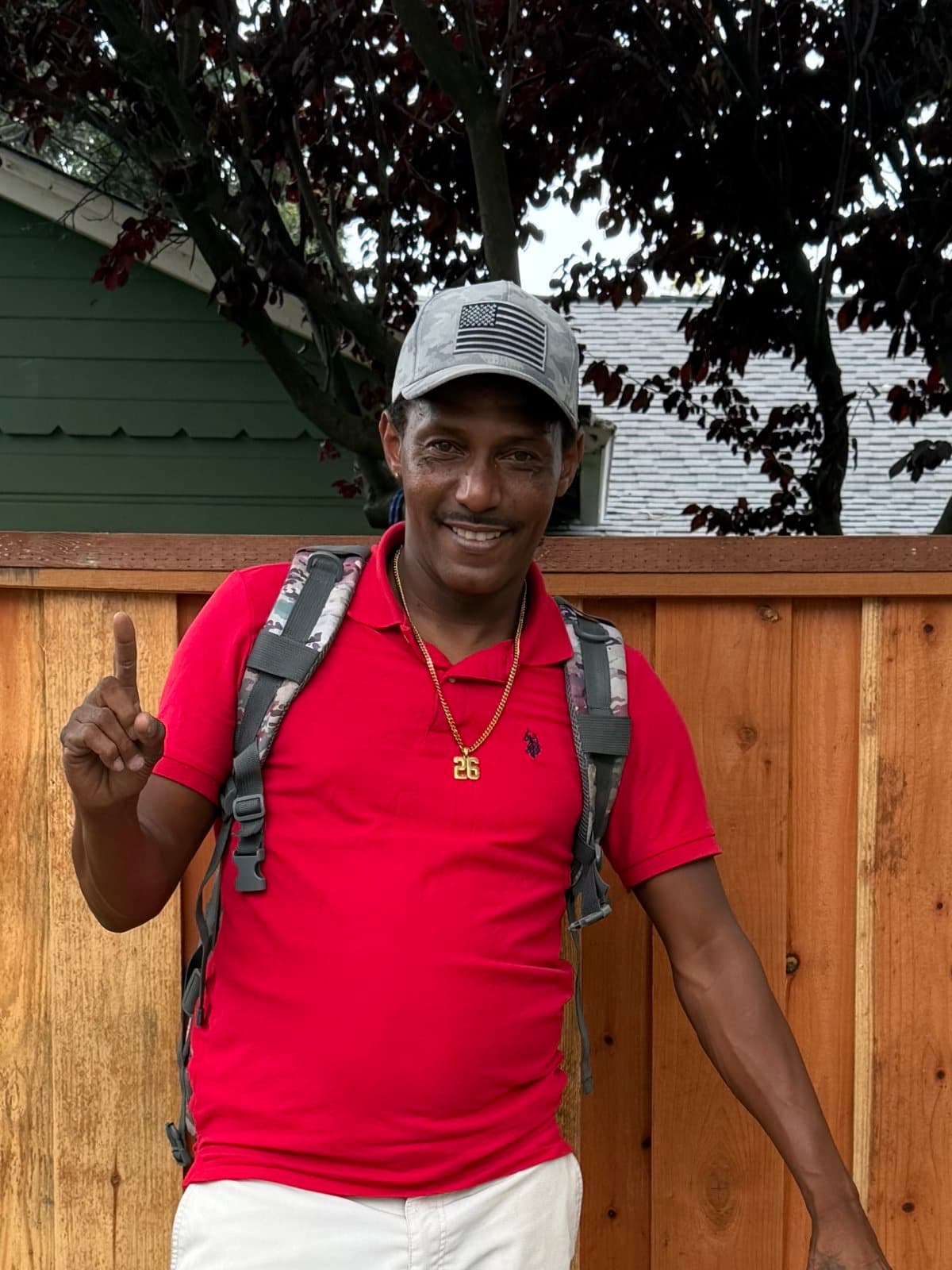 Deonte in a red polo and a gray cap, smiling and holding up one finger